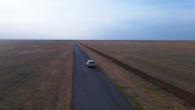 汽车在农村收获的农田中间的荒芜道路上行驶，无人机从不同角度从高处射击。穿越废弃的荒野之旅