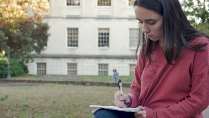 年轻女子用笔在大学校园外面的笔记本上写字