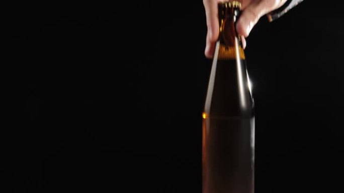 新鲜啤酒。手将带有美味精酿啤酒的棕色瓶子放在黑色背景下的木制桌子上。水滴冷新鲜啤酒。准备喝酒。4K