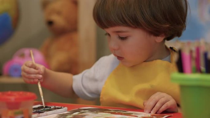 四岁的高加索男孩玩得开心，在纸上画画，富有创造性和艺术性。用彩色颜料在纸上特写肖像儿童画。可爱的小男