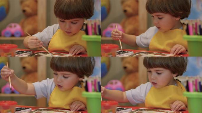 四岁的高加索男孩玩得开心，在纸上画画，富有创造性和艺术性。用彩色颜料在纸上特写肖像儿童画。可爱的小男