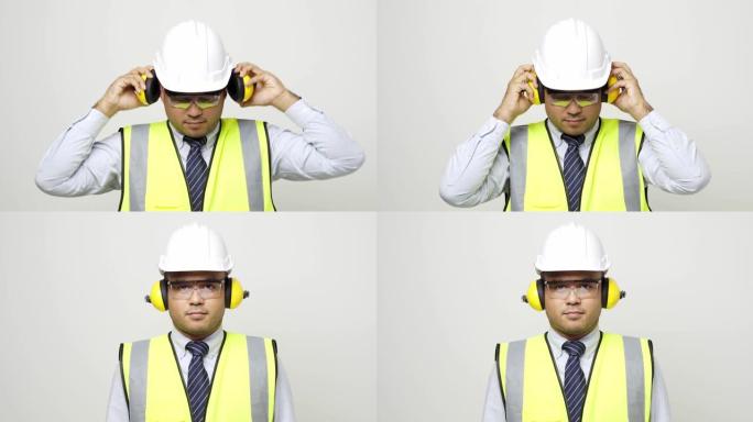 年轻的亚洲土木工程师穿着统一的耳罩头盔安全眼镜站在工作室孤立的白色背景。4k分辨率。