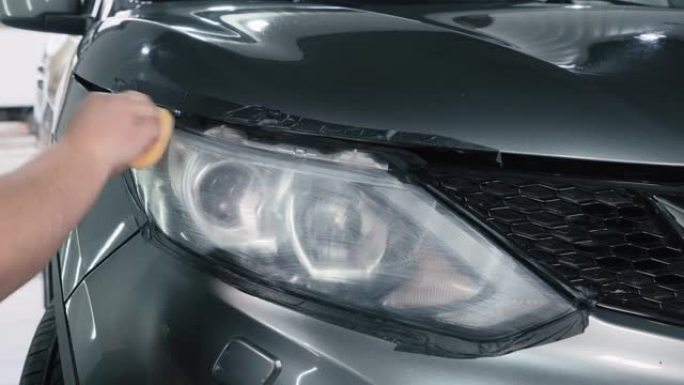 汽车细节。抛光机用海绵将特殊的抛光剂或糊剂或蜡涂在汽车前照灯的光学元件上，特写