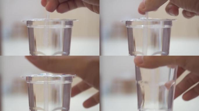 近距离手持吸管刺穿水杯的塑料盖。一次性使用外卖水杯。