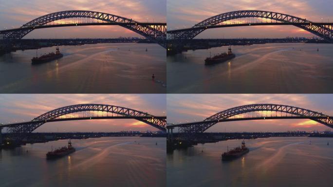 日落时分，一艘商业船只从连接新泽西州和纽约州的贝永大桥下驶过。航拍视频与平移摄像机运动。
