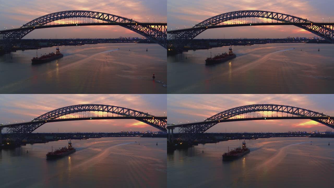 日落时分，一艘商业船只从连接新泽西州和纽约州的贝永大桥下驶过。航拍视频与平移摄像机运动。