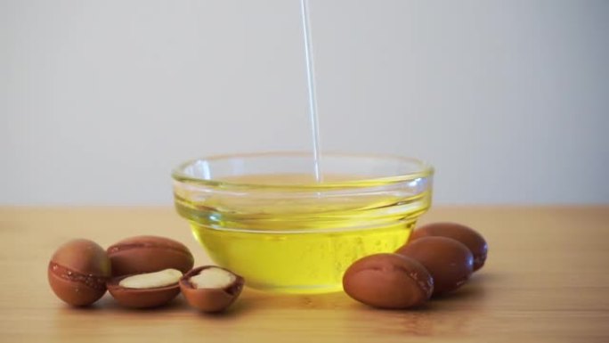 将摩洛哥坚果油倒入带有白色背景上的摩洛哥坚果籽的玻璃碗中。基于摩洛哥坚果油的化妆品概念。