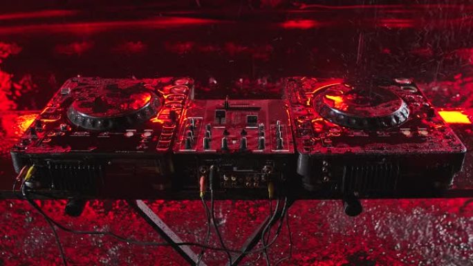 音频混合控制器站在红色照明的黑暗工作室中。DJ工具在倾盆大雨中。顶视图。特写。慢动作