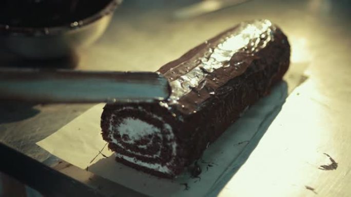 厨师轻拍浸泡海绵蛋糕，均匀涂抹融化的巧克力。