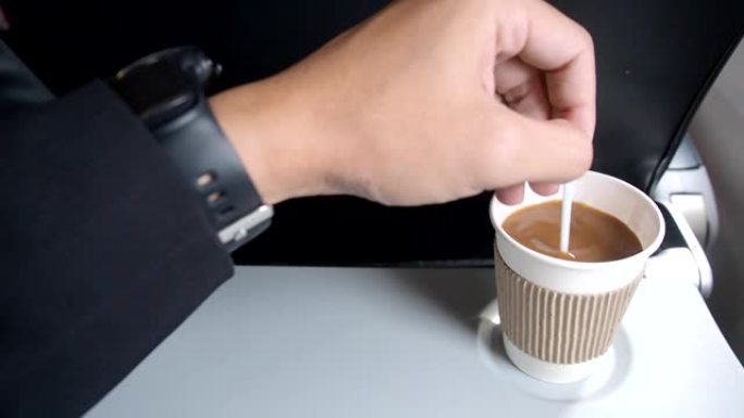 男性的手搅拌咖啡并提起饮料。飞机靠窗座位托盘桌上的咖啡杯。