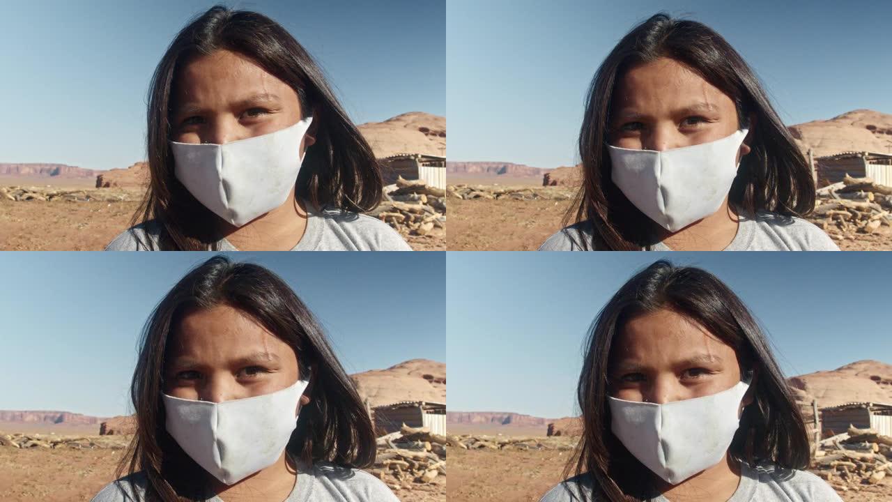 亚利桑那州北部沙漠中的一个年轻的纳瓦霍裔印第安男孩看起来很严肃，穿着新型冠状病毒肺炎的面具，背景是纪