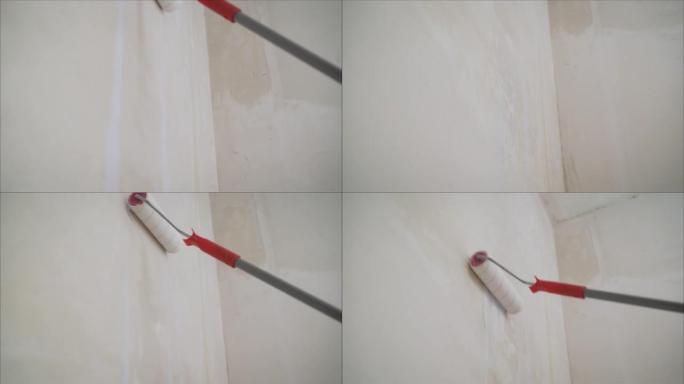 用底漆润滑墙壁。一名工人用白色底漆填充墙壁。油漆滚筒和底漆 ..油漆滚筒靠着空白的白色墙壁站立的背景