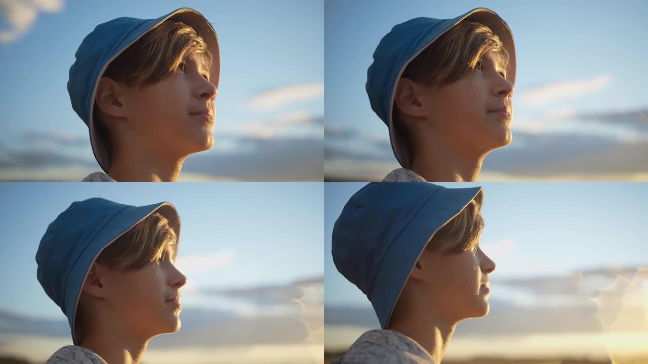 戴着帽子的快乐男孩的肖像看着美丽的蓝天，阳光刺眼