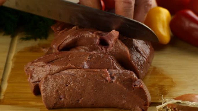 厨师的手用锋利的菜刀在木制厨房板上切生牛肝。