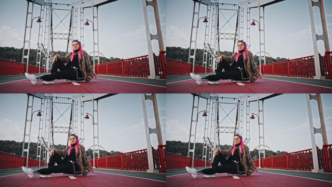 穿着非正式服装的粉红色头发的华丽时髦女人侧身坐在滑板上，在桥上摆姿势