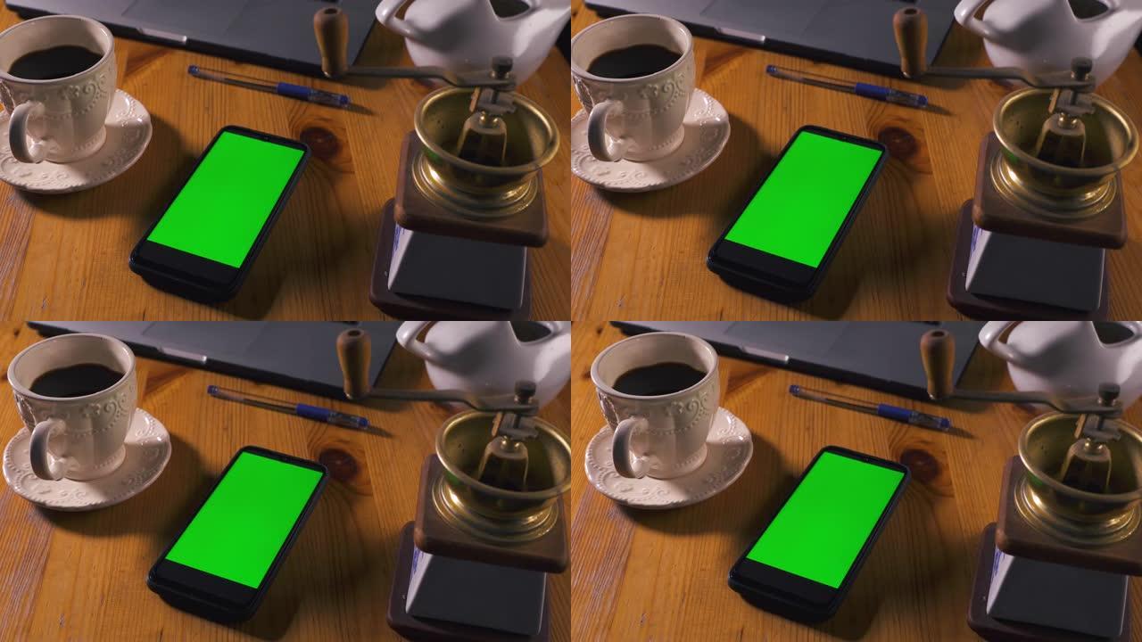 桌子上有绿屏的智能手机。带有绿色屏幕的模型，用于跟踪内容特写。带触摸屏的手机放在一张带笔记本电脑和一