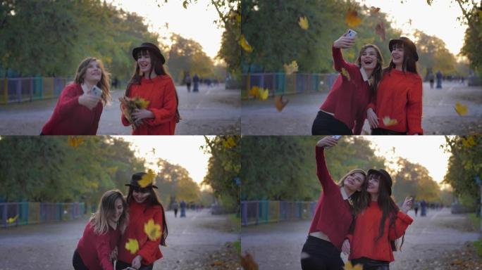 穿着红色衣服的迷人年轻女性在手机上被拍到，手里拿着树叶，然后把它们扔起来，在落叶的背景下自拍