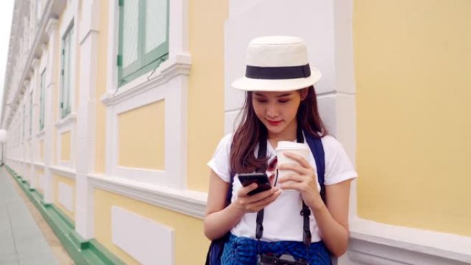 20-30岁的女性站在墙边，手里拿着一杯热可可和一部手机，预约与朋友分享地点。