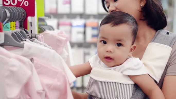 一个亚洲男婴和他的母亲在一家儿童服装店抱着。