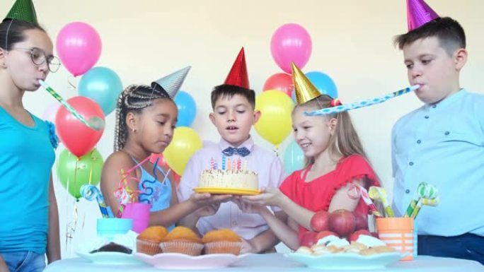 小男孩吹蜡烛，而朋友在生日时拿着蛋糕