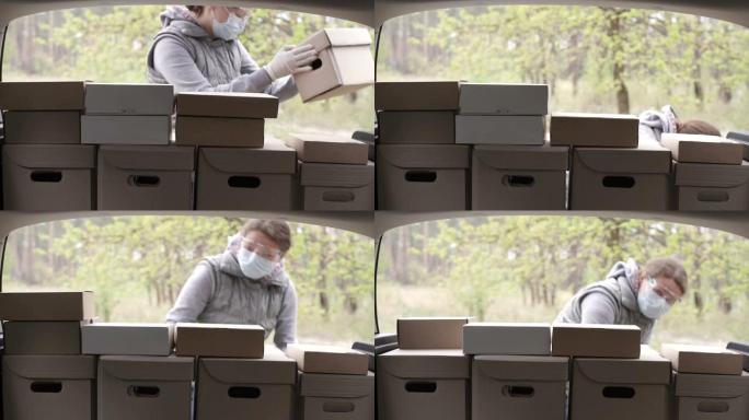 一名穿着防护服的志愿者将箱子装入汽车后备箱。冠状病毒大流行期间为家庭工作和社会距离提供送餐服务。网上