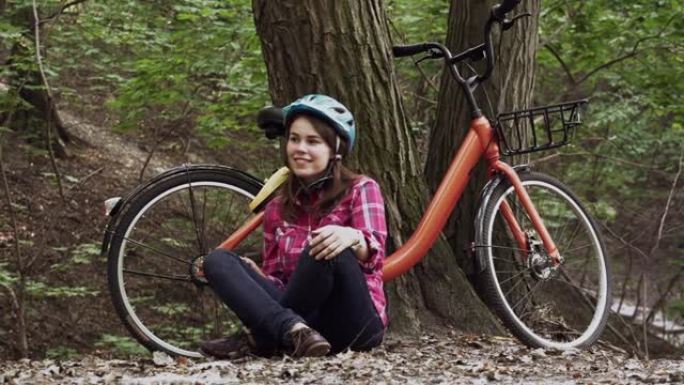 主题生态自行车运输。穿着牛仔裤和衬衫的年轻白人妇女学生坐在公园附近的橙色自行车租赁休息。骑自行车后休
