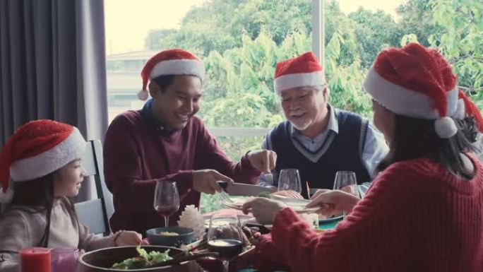戴着红帽子的亚洲家庭，在餐厅的大桌子上用餐或用餐