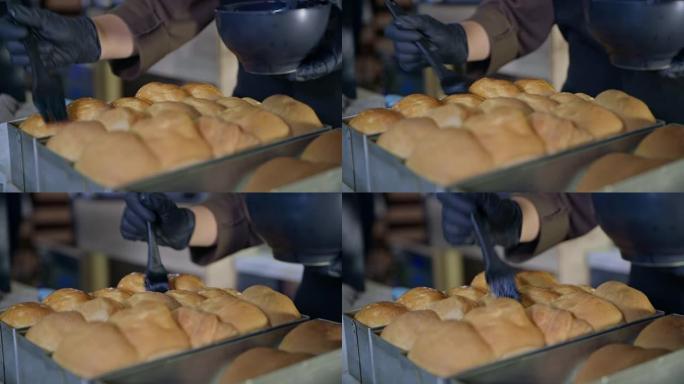 糕点，带手套的女面包师用硅胶糕点刷涂抹新鲜热的，带喙的新鲜小麦粉的香香面包，特写