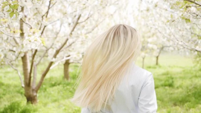 美丽的金发女郎跑过盛开的樱桃花园。