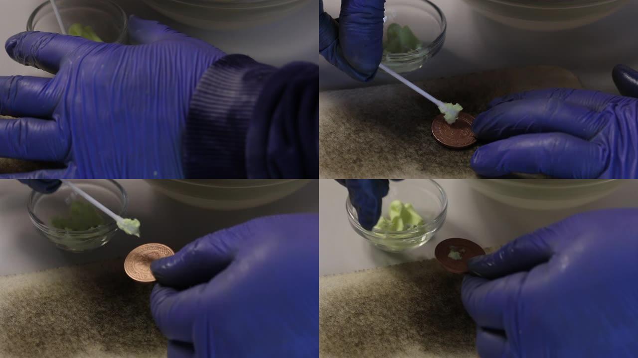 从腐蚀中清除的硬币放在一块毛毡上。一个戴着橡胶手套的人在硬币上涂上硫磺软膏。用硫酸软膏制铜币。