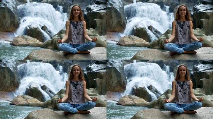 金发女孩在瑜伽姿势在石头上对着瀑布