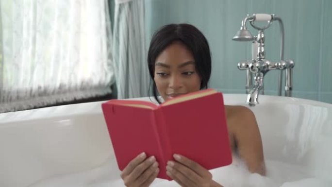 泡泡浴中的非洲年轻女子阅读红皮书。休闲和生活方式概念