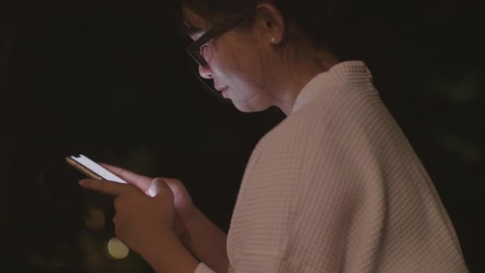 戴着眼镜坐着的亚洲妇女使用她的智能手机。