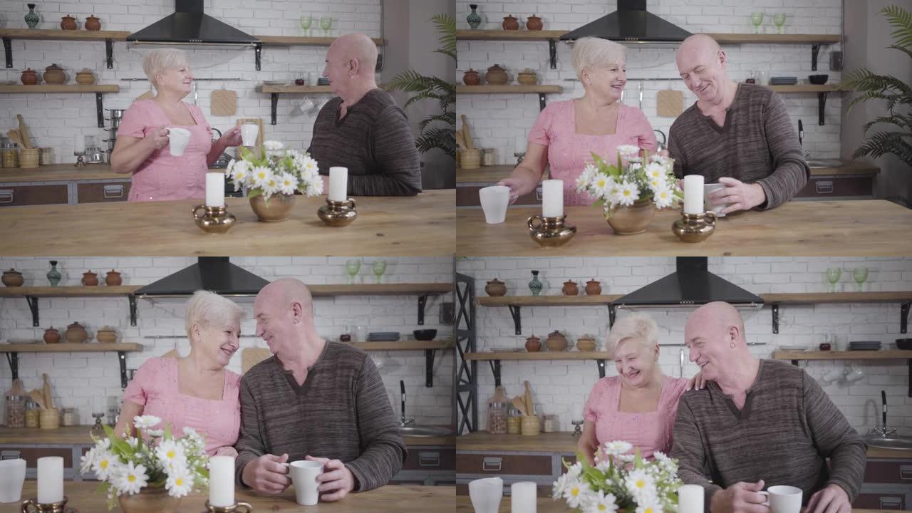 快乐的白人老太太从厨房带白杯茶或咖啡，和她可爱的丈夫聊天。微笑的高级夫妇在家休息。永恒的爱，幸福，舒