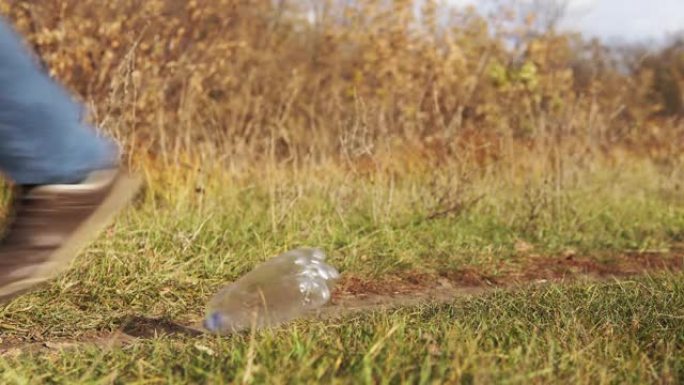 生态概念塑料污染。一个不负责任的穿着蓝色牛仔裤的男人把塑料瓶扔到公园的绿草地上。