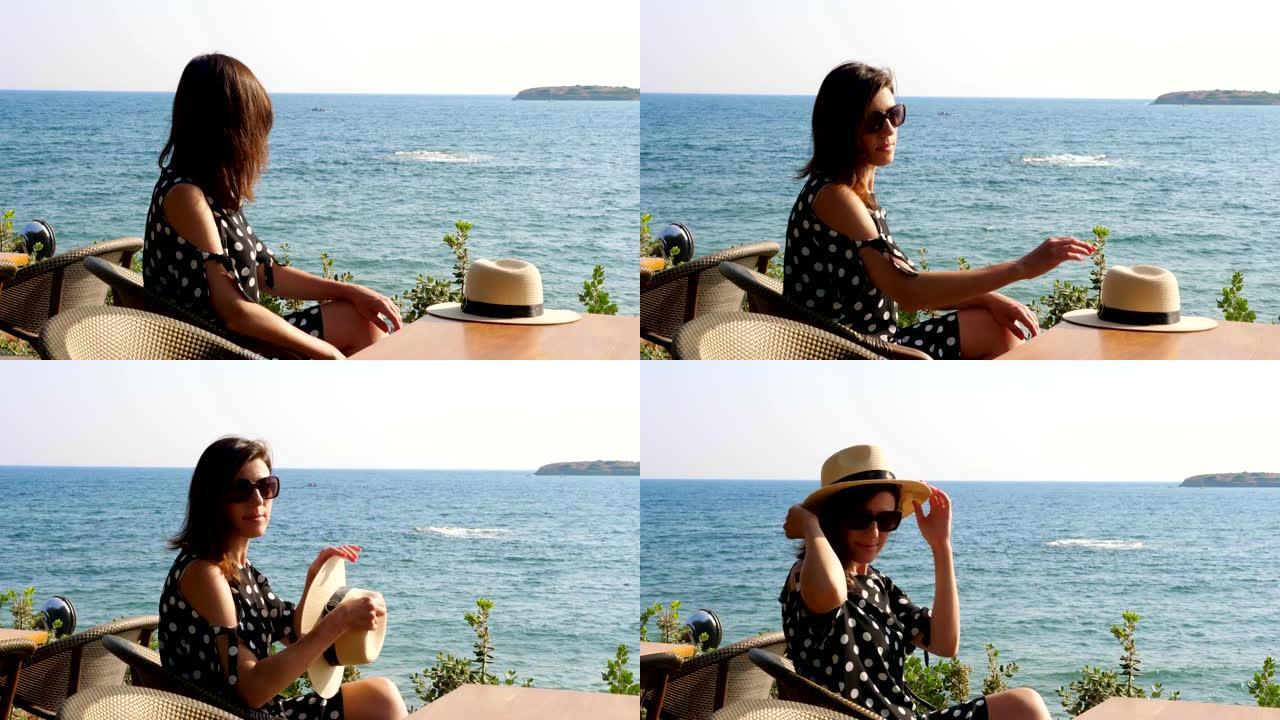 黑发女孩坐在海边咖啡馆的桌子旁，欣赏海景。炎热的夏日