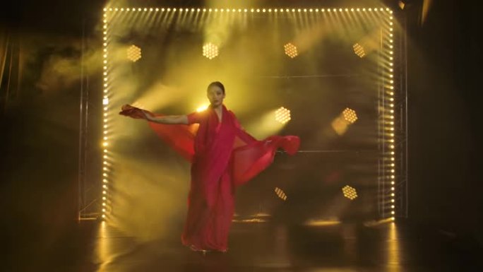 一个穿着红色纱丽的年轻女孩舞者。印度民间舞蹈。在黑暗的工作室里拍摄，有烟雾和黄色霓虹灯。慢动作