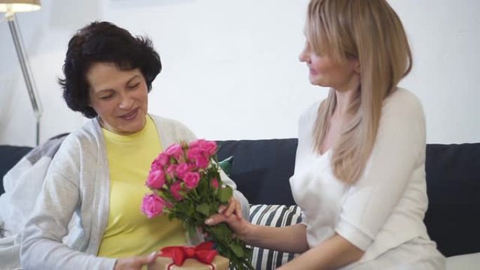 年轻迷人的女儿正在拜访年迈的母亲，交谈并赠送美丽的粉红玫瑰