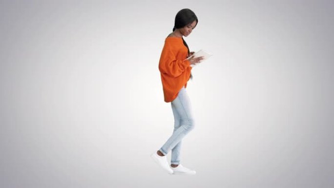 微笑的非洲裔美国妇女在渐变背景上行走时使用平板电脑