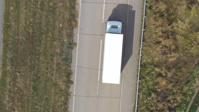 白色货运拖车在空旷的道路上行驶并运输货物的卡车的鸟瞰图。飞越一辆通过乡村高速公路的送货卡车。物流概念