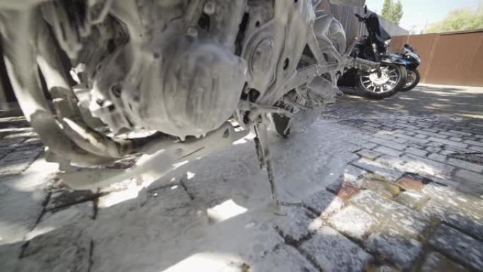 男子的慢动作镜头从泥土中清洗摩托车。喷水和泡沫的特写镜头