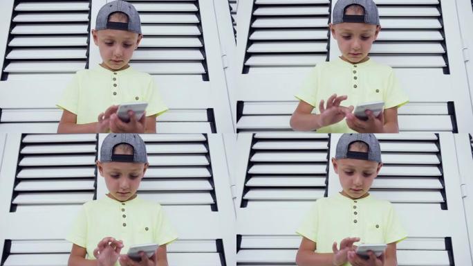 年轻的少年在智能手机上玩游戏，孤立在白门背景上。玩智能手机技术的孩子。在智能手机上写信息的小男孩的特