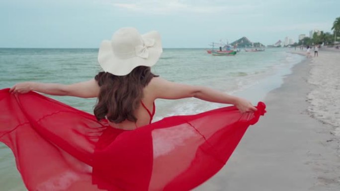 穿着红色连衣裙的快乐女人在海边散步的慢动作