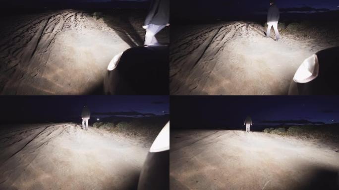 一个人在晚上走在沙滩上，远离汽车的前灯
