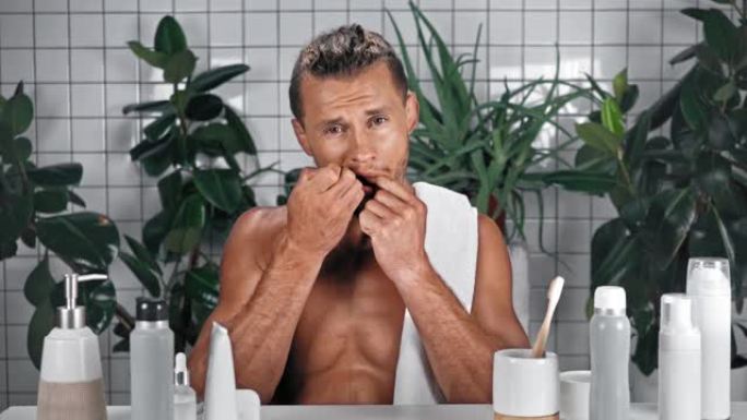 男人在浴室使用牙线并露出牙齿