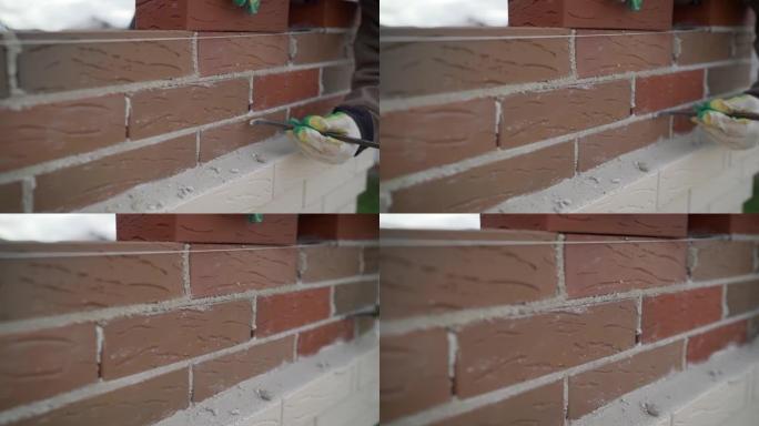 工人小心翼翼地做砖墙。工人擦墙砖。工人擦拭砖块之间的接缝。熟练工匠铺设红砖大砖石的特写。建筑概念