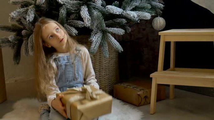 可爱的金发女孩收到了一个礼品盒，装在圣诞树、快乐的童年和圣诞庆祝概念附近的工艺纸包装