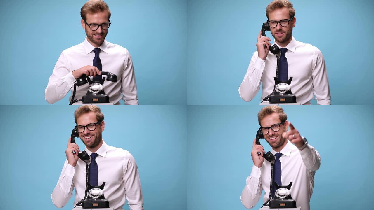 有吸引力的商人拿起电话，说话，大笑，指着蓝色背景上的相机