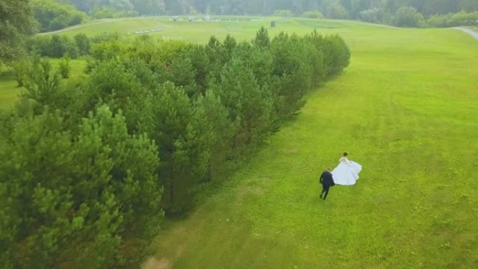 新郎在伍德鸟瞰图的绿色田野中跟随新娘奔跑
