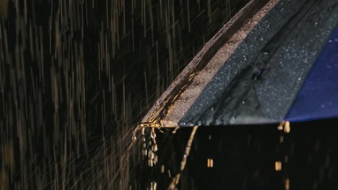 雨水从潮湿的雨伞中流下。水滴在黑色背景下的演播室灯光中闪闪发光。以慢动作拍摄特写镜头